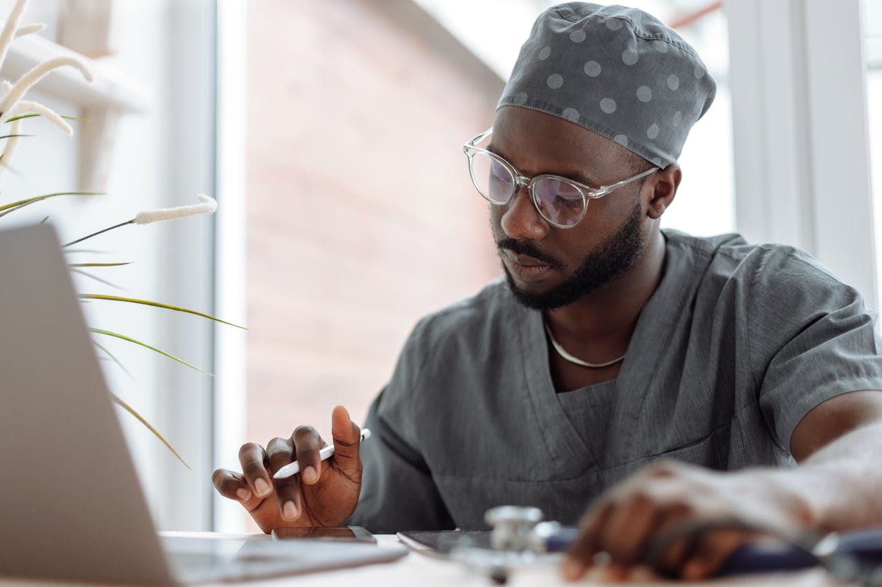 A focused male doctor in scrubs working on a laptop, showcasing professionalism and modern healthcare technology.