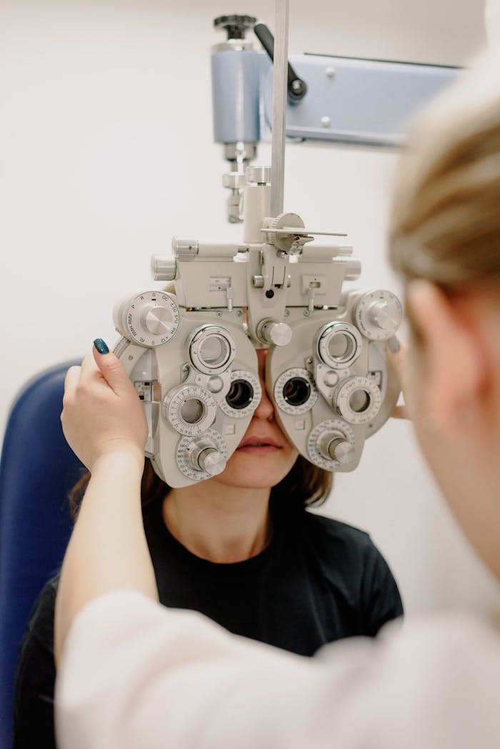 An optometrist conducts an eye exam with a phoropter on a female patient.